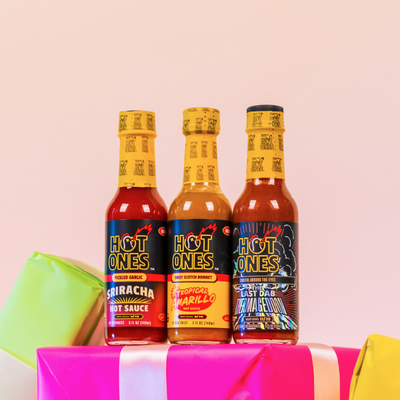 Three bottles of Hot Ones hot sauce on a colorful background